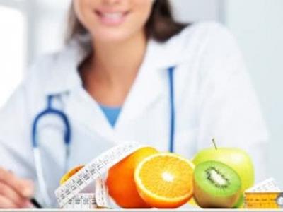 A imagem mostra uma nutricionista sentada com frutas em cima da mesa