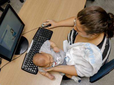 Imagem mostra mãe com bebê em frente ao computador