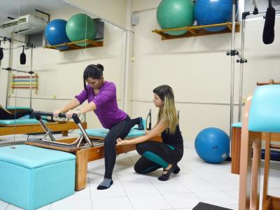 Imagem mostra mulher fazendo exercício de pilates com auxilio de instrutora